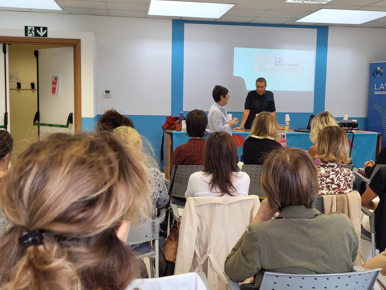 aula con donne sedute e due formatrici davanti al videoproiettore Strategie di investimento per il successo delle startup femminili